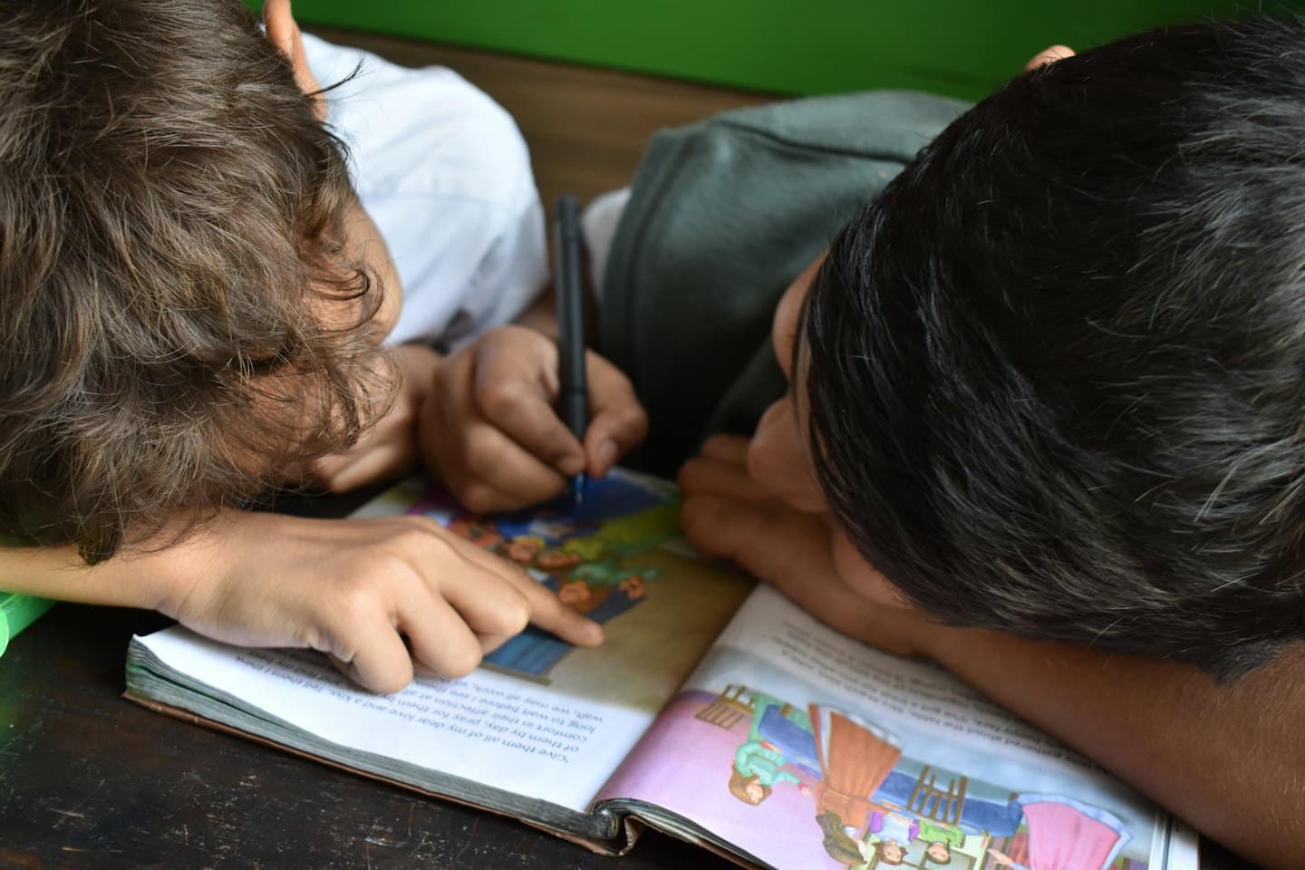 Dos niños dibujando y leyendo un libro abierto juntos.